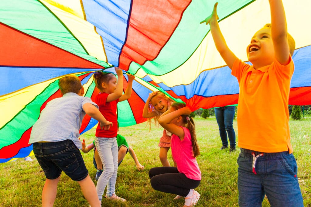 Close up view of children playing hide-and-seek under the huge rainbow cover