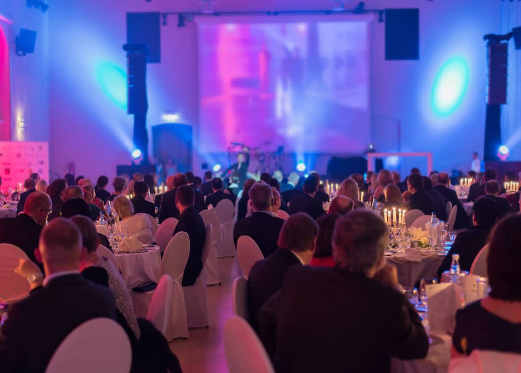 tables of attendees at a formal gala, illuminated with purple, pink, and blue lights