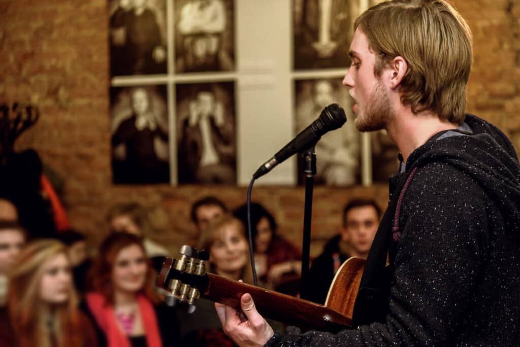 stylish vocalist with beard performing lyrical song on stage with his band for an audience