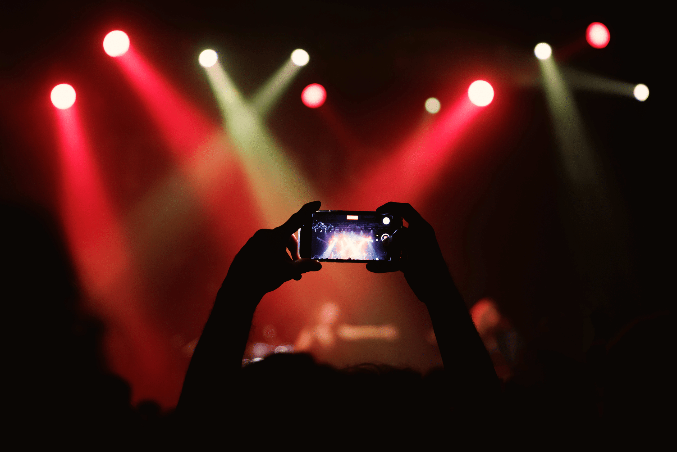 fan filming a concert on her phone with red stage lights in the background