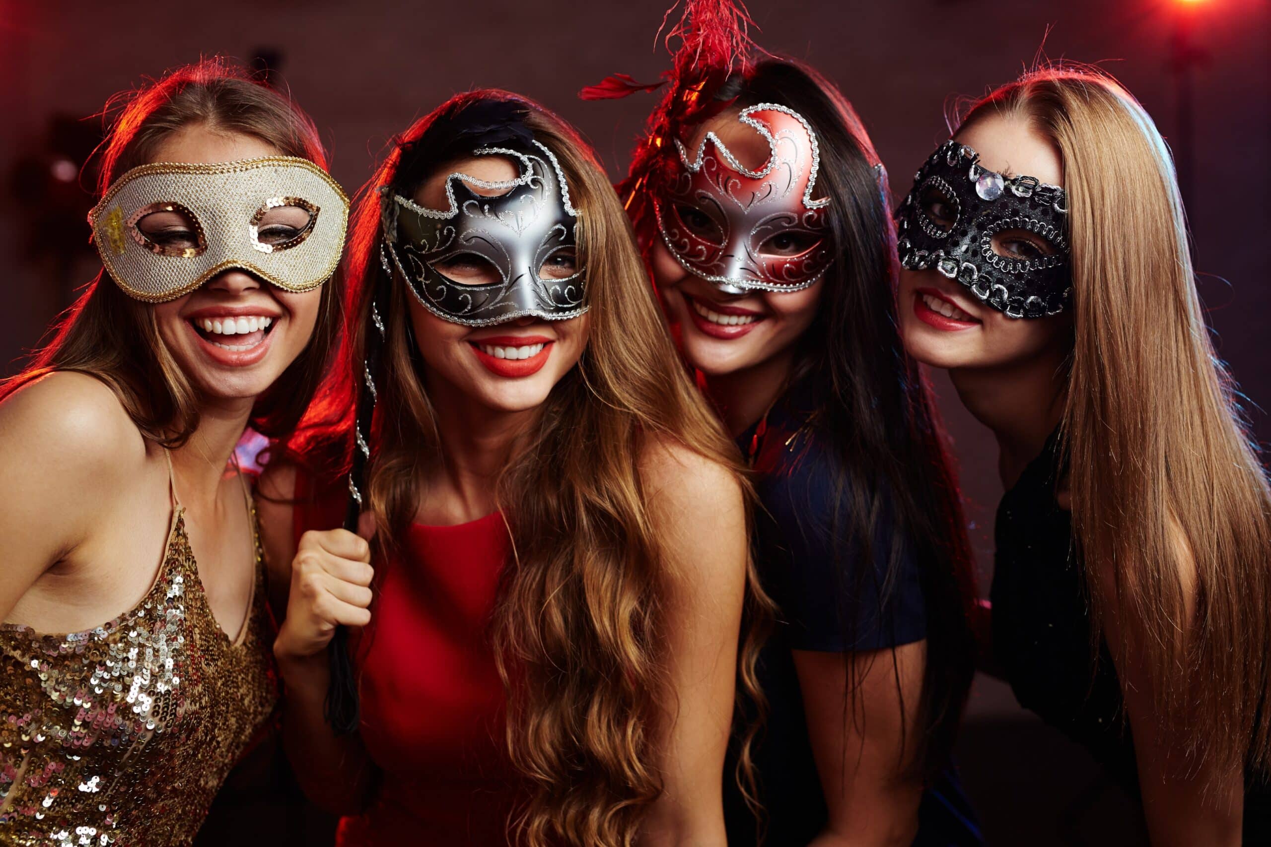 A group of friends at a masquerade ball holding up their masks for a picture