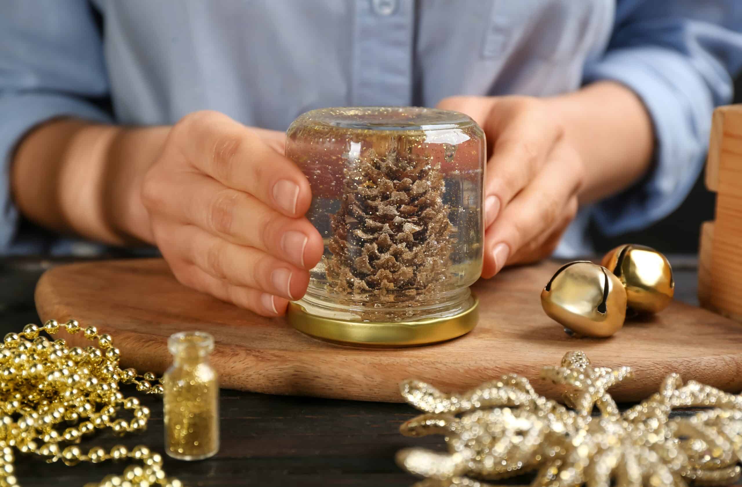 A person holding their do-it-yourself snow globe that has a pinecone and gold glitter in it